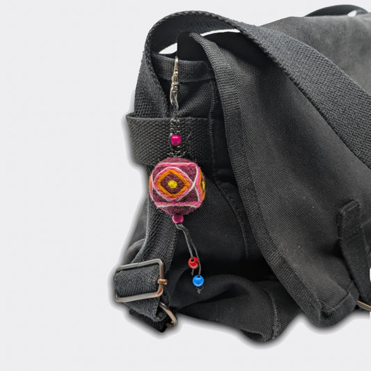 Porte-clé décoratif Bogdan constitué d'une boule en feutre rouge foncé avec traits jaunes accroché à un sac