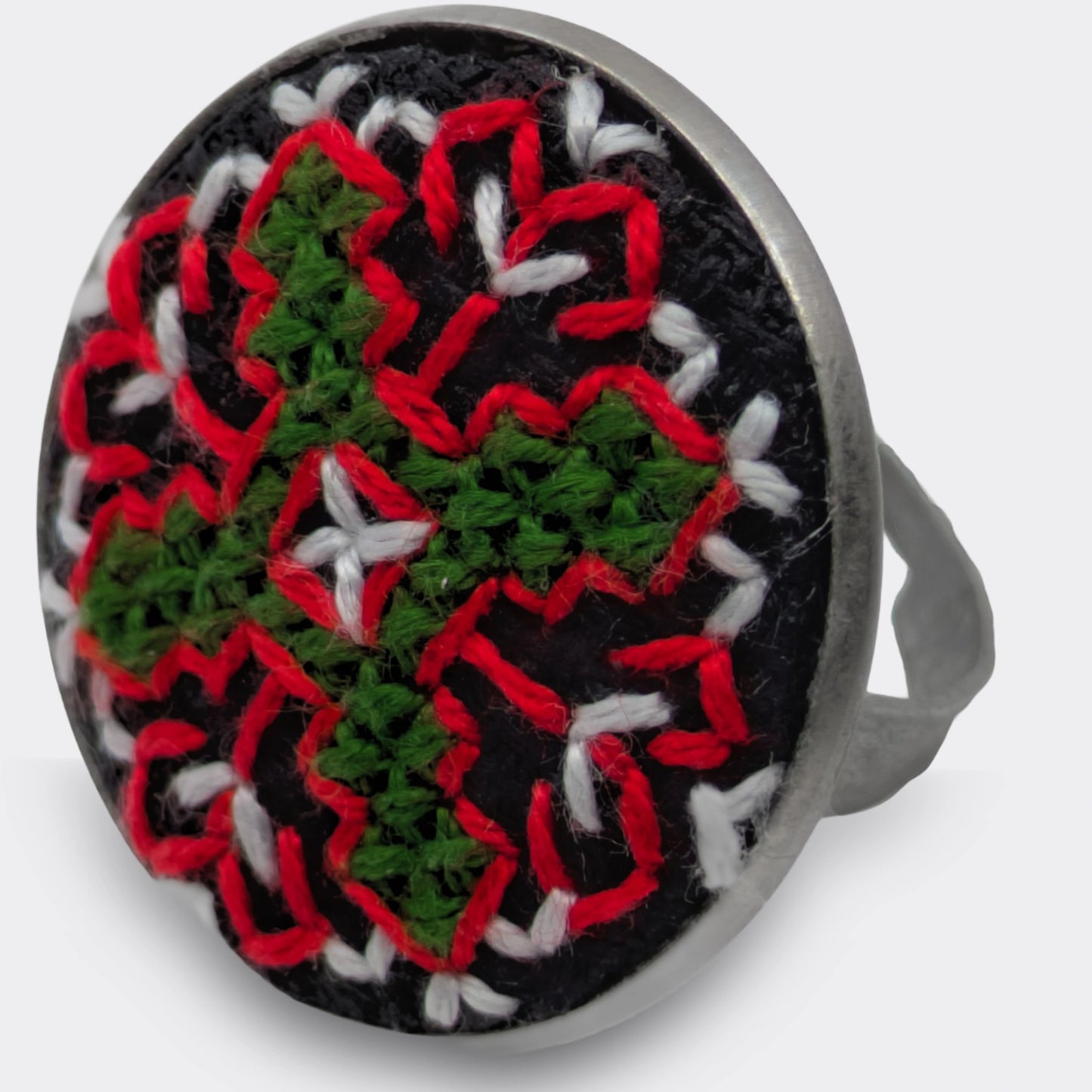 Détail d'une bague brodée avec motif coloré sur tissu panama. Le plateau rond met en valeur la broderie inspirée du Kosovo.