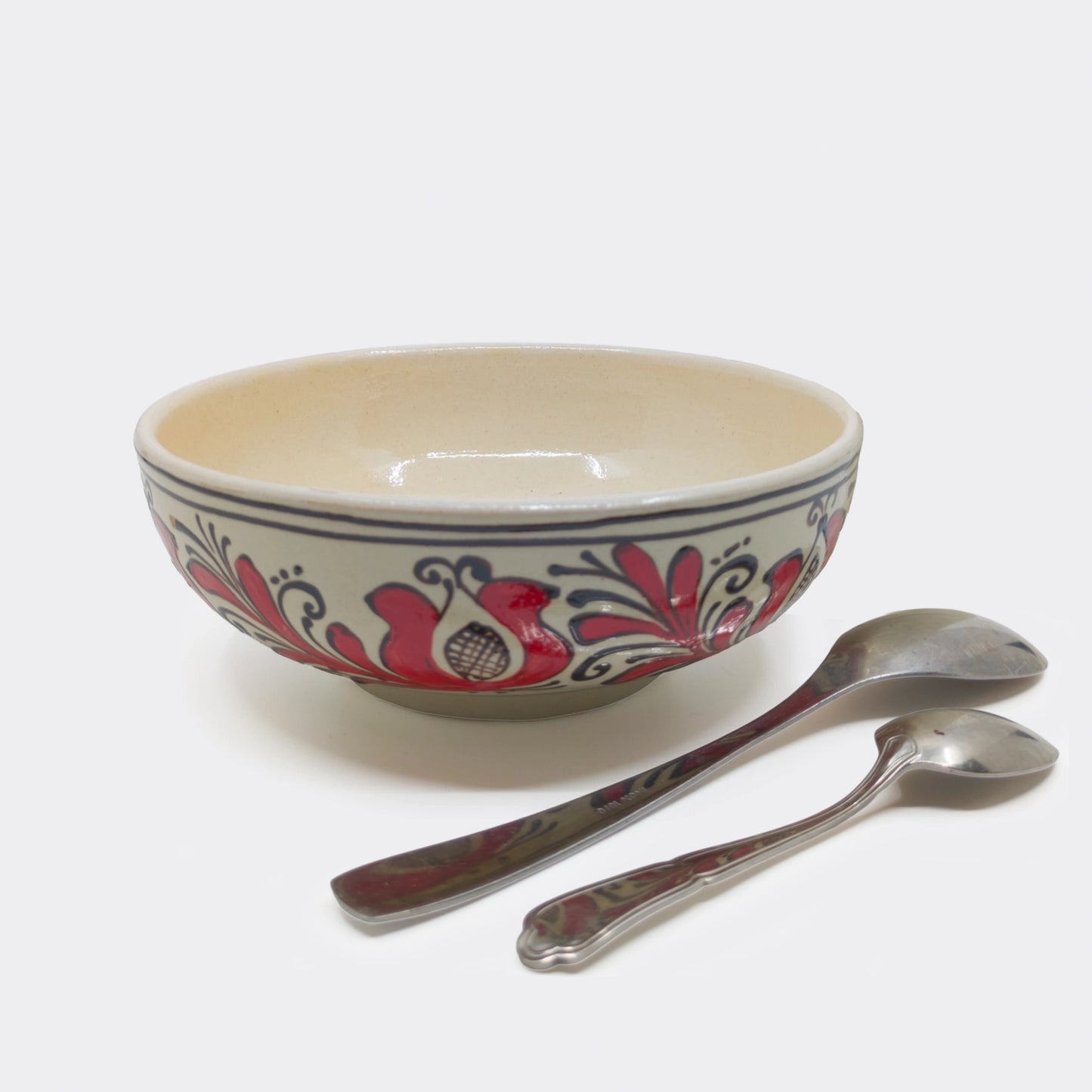 Grand bol en céramique de Corund présenté avec couverts, fond crème et motifs rouges traditionnels. Bol artisanal roumain 18 cm.