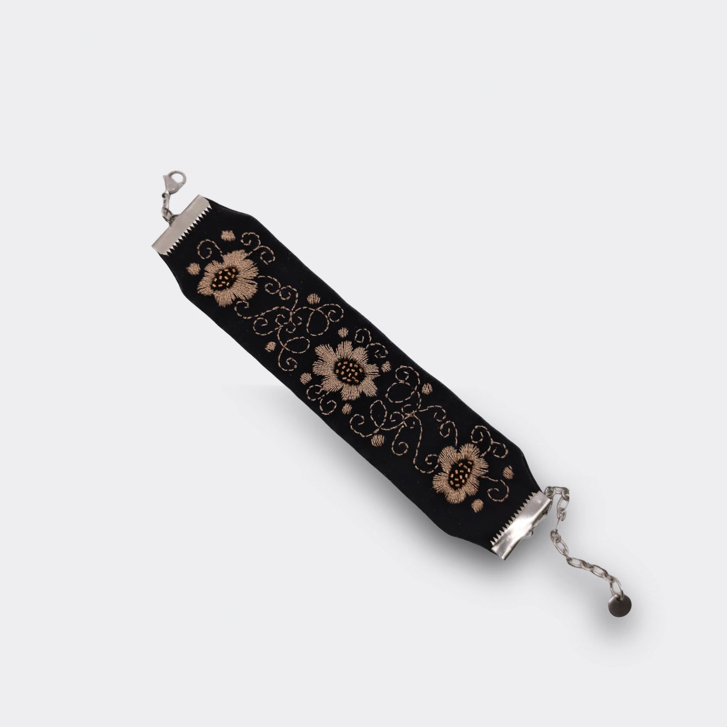 Gros plan sur la broderie champagne d’un bracelet textile noir, décor floral stylisé réalisé à la main. Bijou artisanal serbe, détail du motif, bracelet déplié