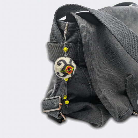 Vue de la breloque Stanislav en feutre, décor tortue traditionnelle rouge et noir. Elle est accrochée sur un sac