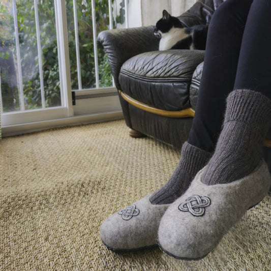 Un nœud de Salomon orne des chaussons en feutre gris, entièrement faits main. Ils sont portés par une personne.