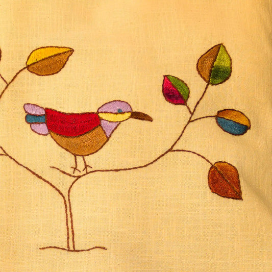 Gros plan sur les feuilles colorées et un oiseau brodés à la main sur une housse de coussin.
