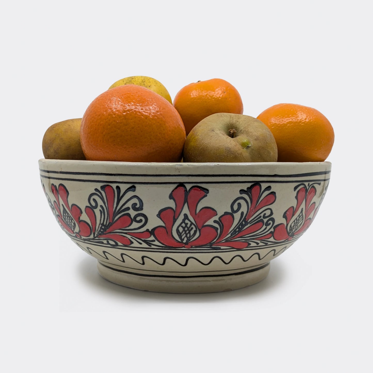 Jatte artisanale de Transylvanie décorée à la main de fleurs rouges et d’une frise simple. Jatte remplie avec des fruits.