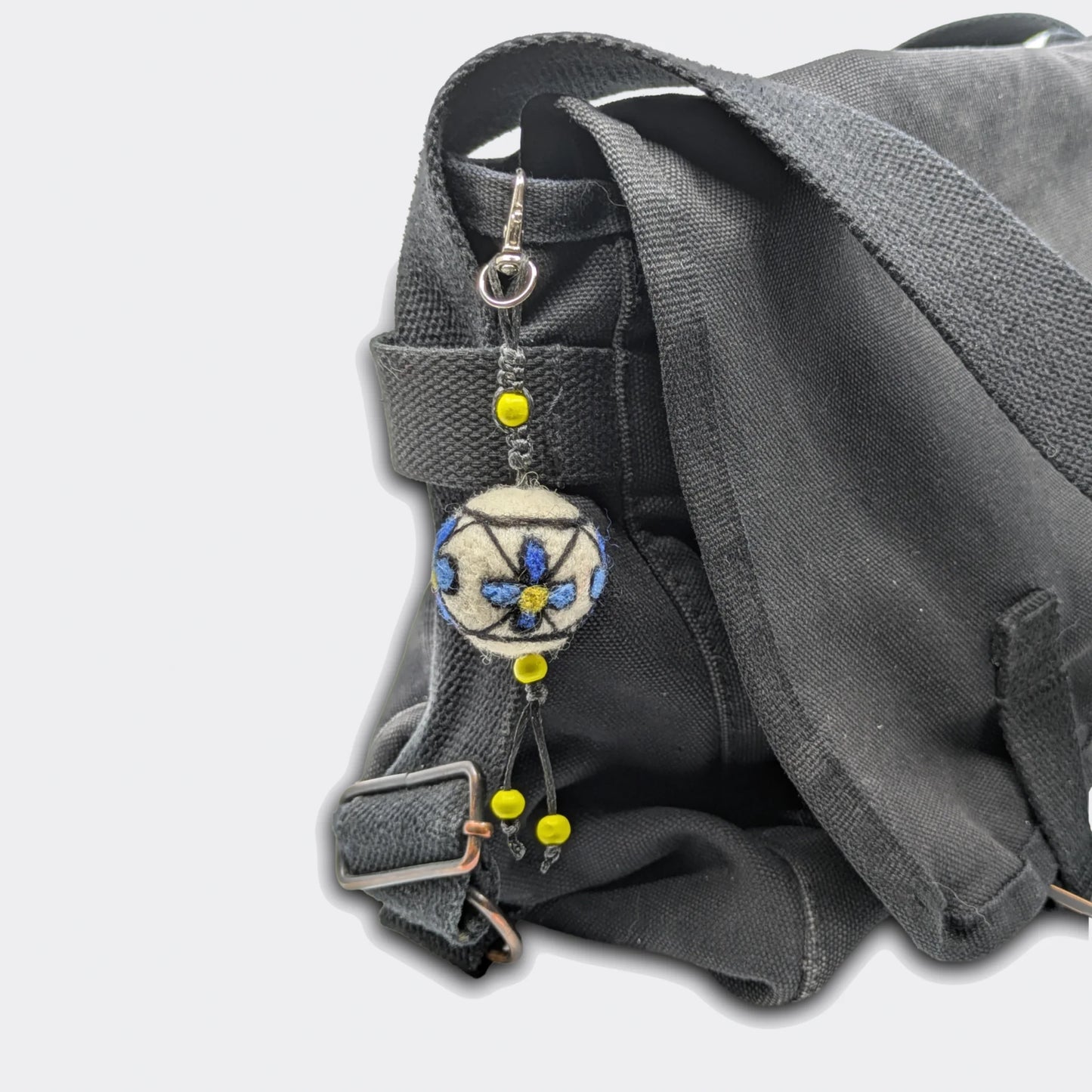 Breloque Milena accrochée sur sac avec boule en feutre décorée de fleurs bleues. Entièrement fait main.