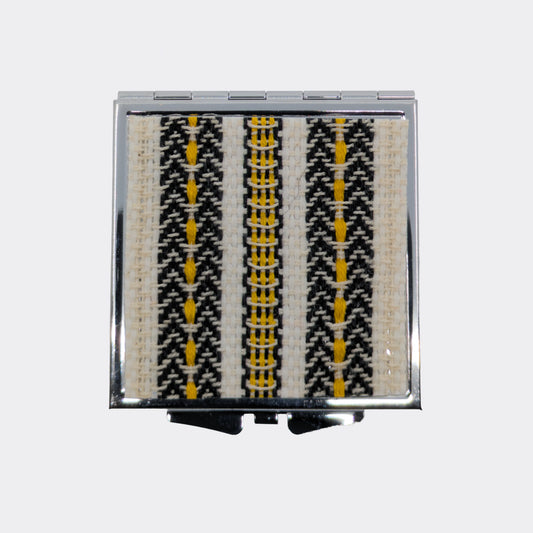 Miroir de poche ouvert avec frises jaunes tissées. Les couleurs évoquent les textiles d’Europe centrale. Parfait pour de petites retouches.