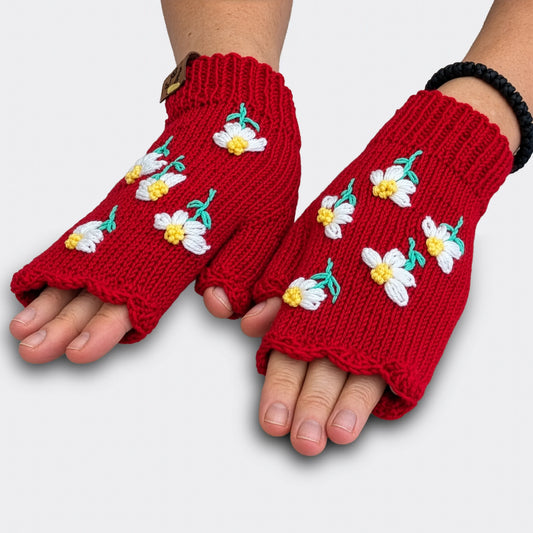 Sur ces mitaines rouges tricotées à la main, des fleurs blanches aux tiges vertes apparaissent séparément. La vue à plat laisse voir les petits motifs floraux et le bord supérieur festonné.