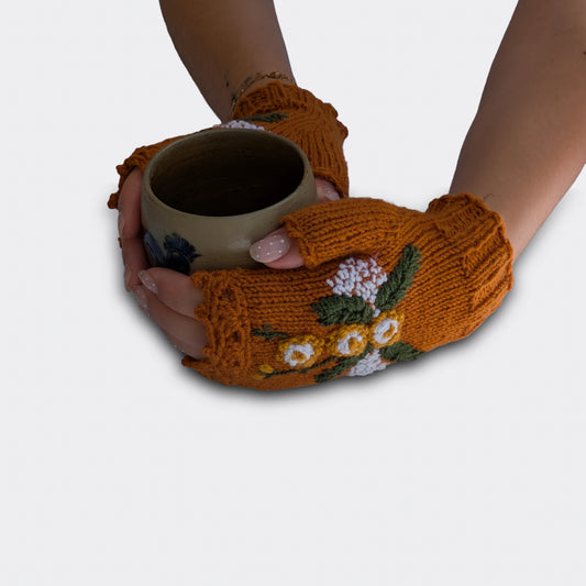 Mitaines brun cuivré tenant une tasse, avec fleurs jaunes et blanches en relief, feuillage vert et fines broderies blanches.
