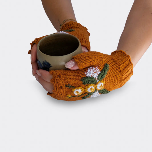 Mitaines brun cuivré tenant une tasse, avec fleurs jaunes et blanches en relief, feuillage vert et fines broderies blanches.