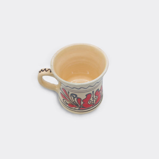 Mug en céramique de Corund vu du dessus, intérieur émaillé crème et bord brut. Tasse artisanale roumaine faite main. Décor floral rouge extérieur.