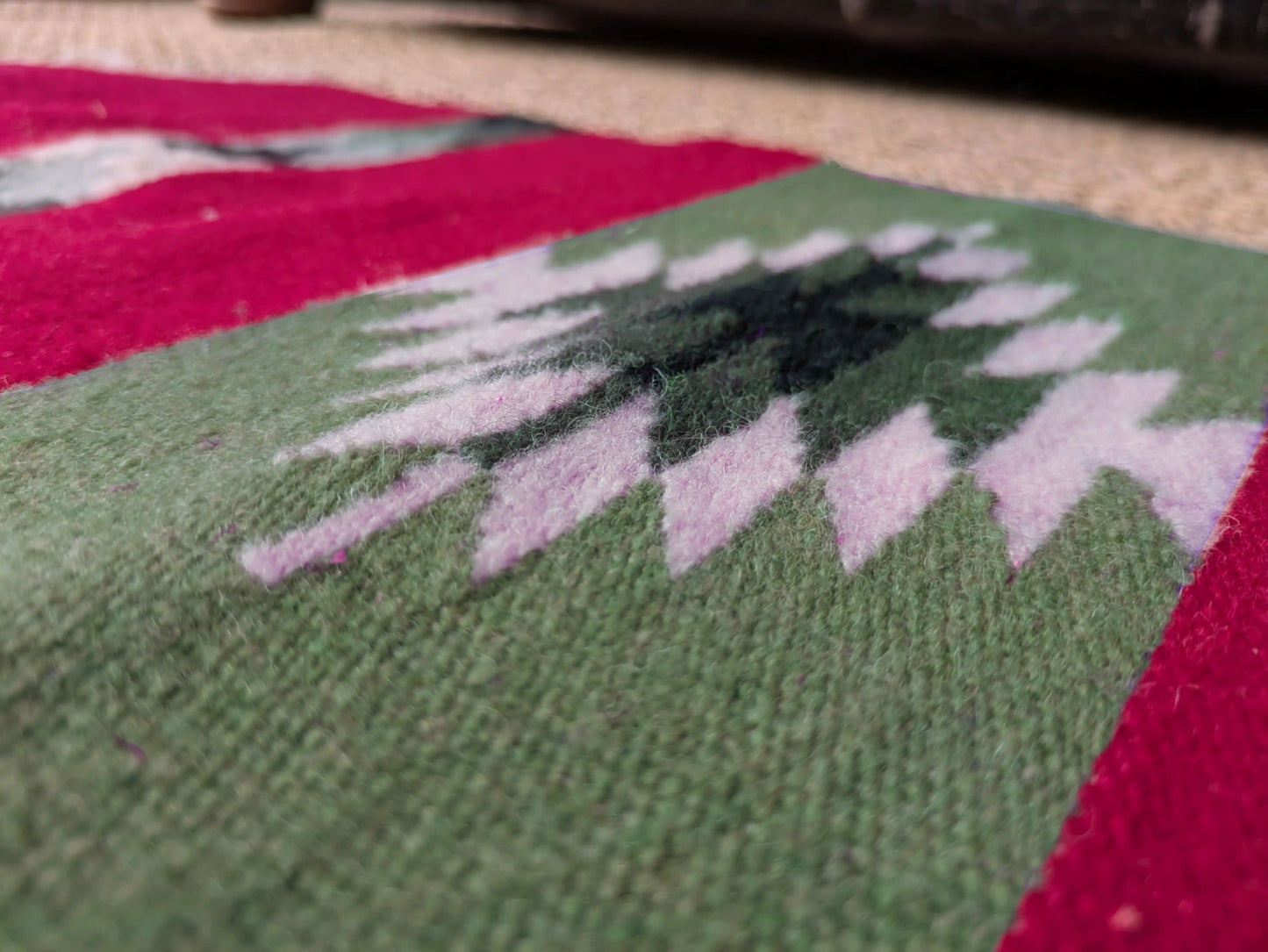 Détail d’un motif géométrique balkanique sur un tapis rouge et vert. Les couleurs contrastées soulignent la construction symétrique.