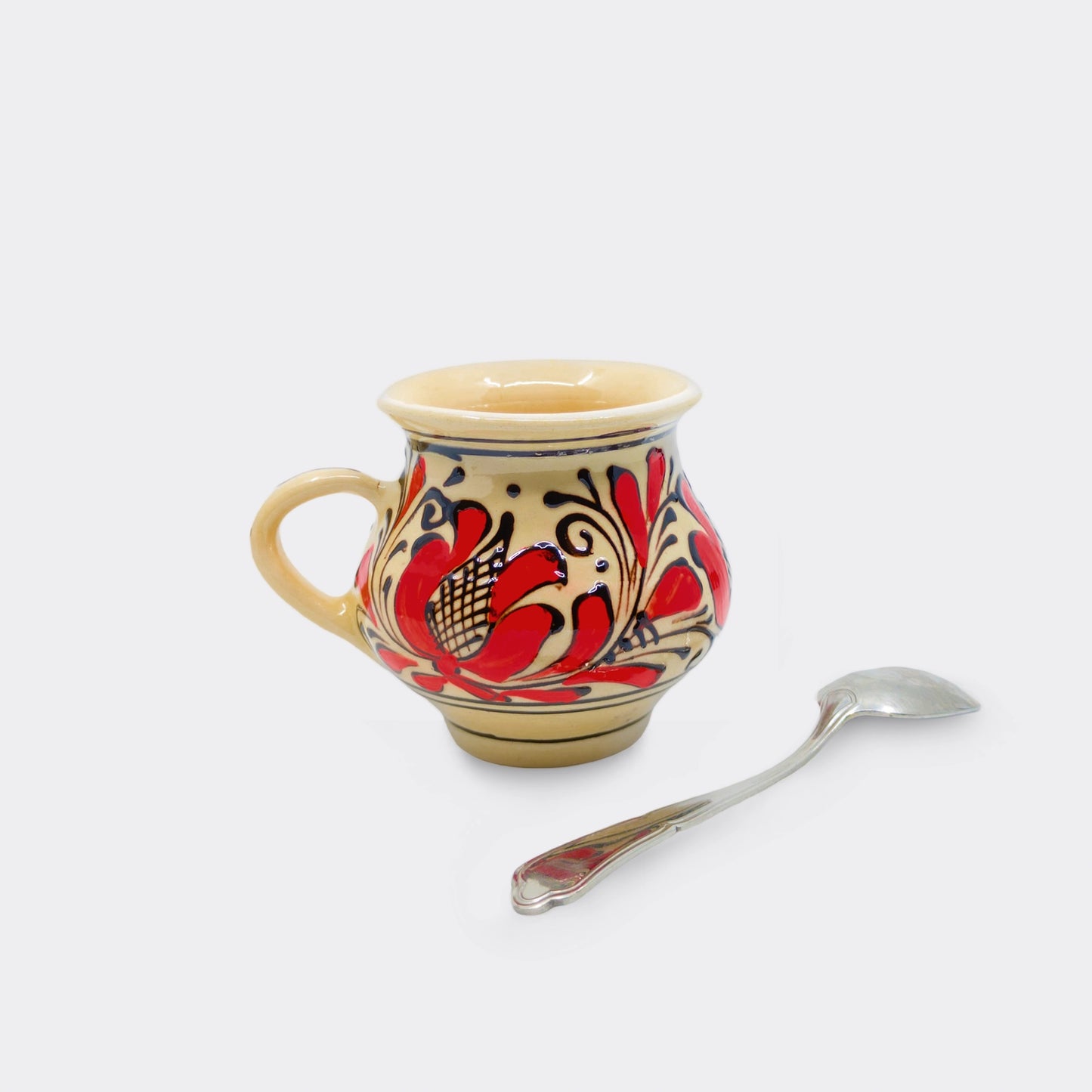 Tasse traditionnelle de Corund au profil bombé, décor floral rouge peint à la main sur céramique artisanale.