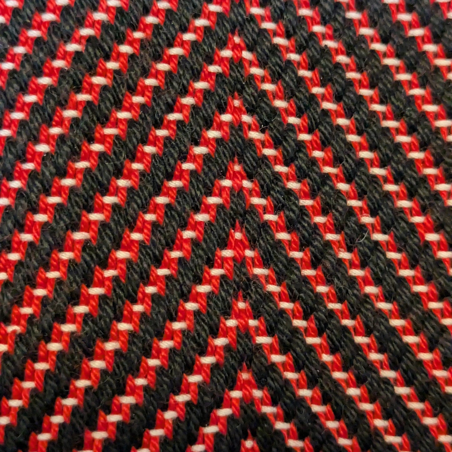 Gros plan du tissage sergé à chevrons, fils noirs épais et fils rouges fins, relief textile doux et régulier, fabrication artisanale.