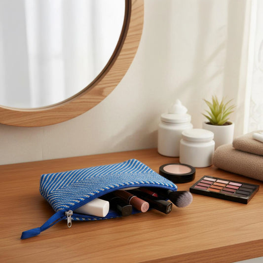 Trousse de toilette artisanale bleue et blanche tissée main, ouverte sur une table de salle de bain, contenant des produits de maquillage.