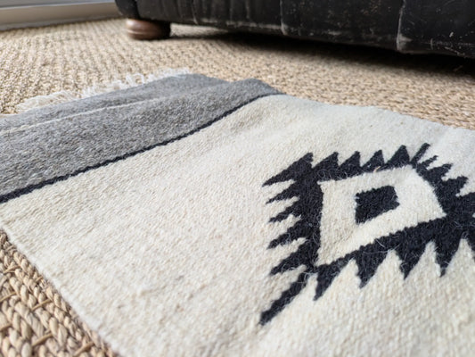 Vue rapprochée d’un tapis balkanique en laine, gris et blanc cassé. Losange traditionnel central encadré par deux bandes grises. Tissage manuel au relief discret.