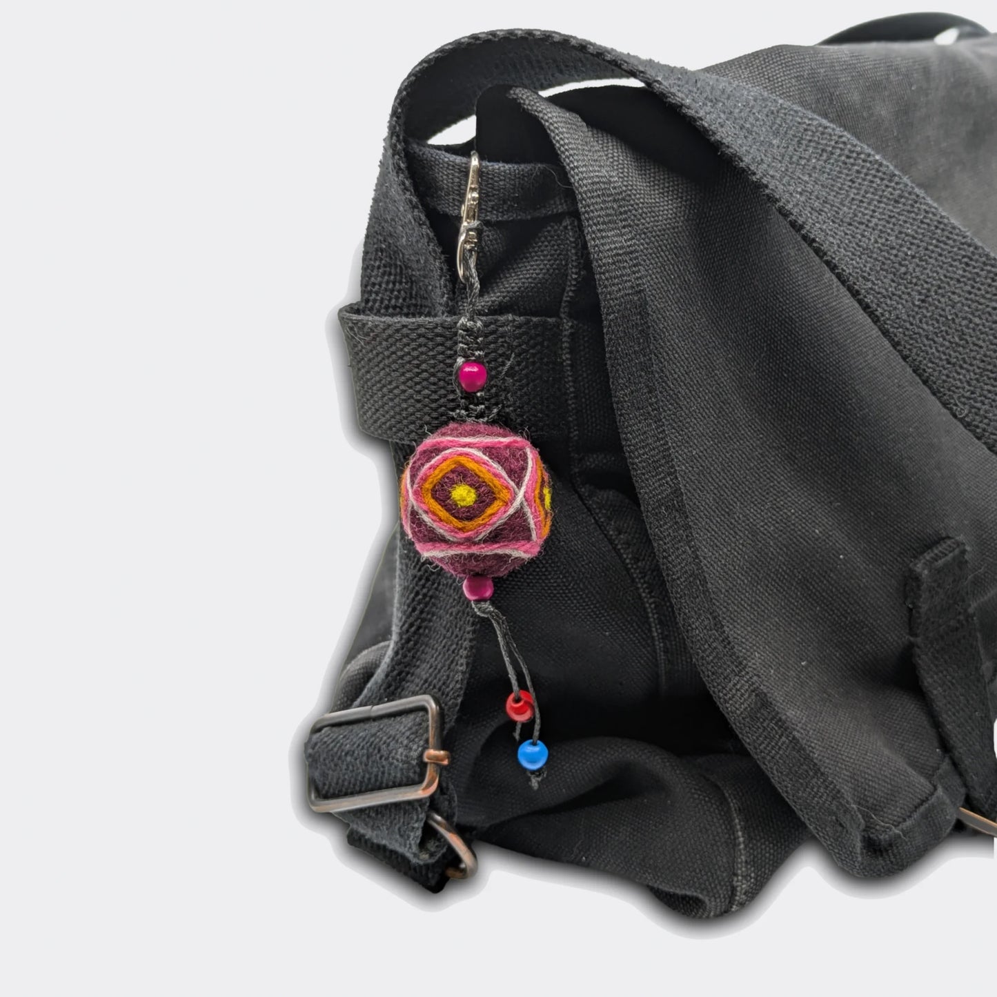 Porte-clé décoratif Bogdan constitué d'une boule en feutre rouge foncé avec traits jaunes accroché à un sac