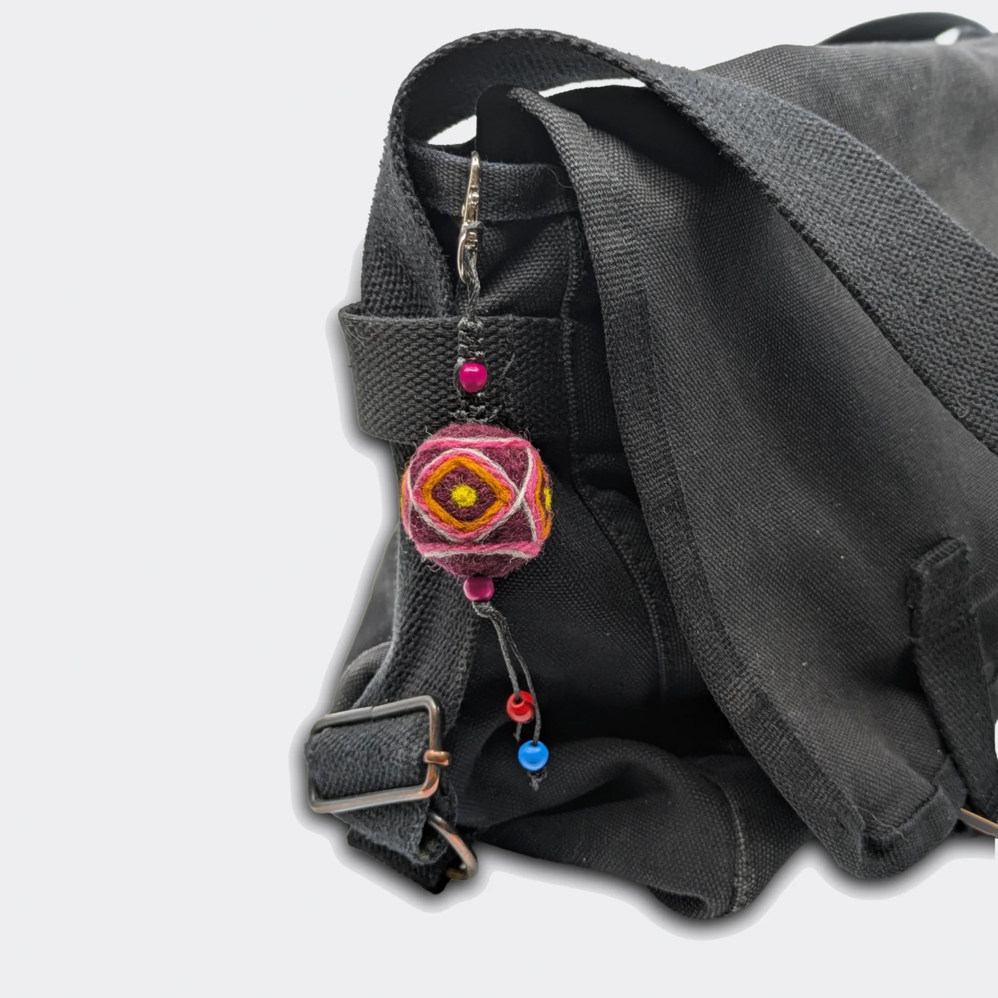 Porte-clé décoratif Bogdan constitué d'une boule en feutre rouge foncé avec traits jaunes accroché à un sac