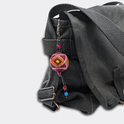 Porte-clé décoratif Bogdan constitué d'une boule en feutre rouge foncé avec traits jaunes accroché à un sac