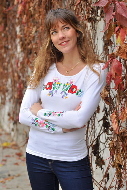 T shirt blanc à manches longues avec des broderies à florales hongroises Kalocsa sur la poitrine et les manches. Vue en entier, un peu en biais.