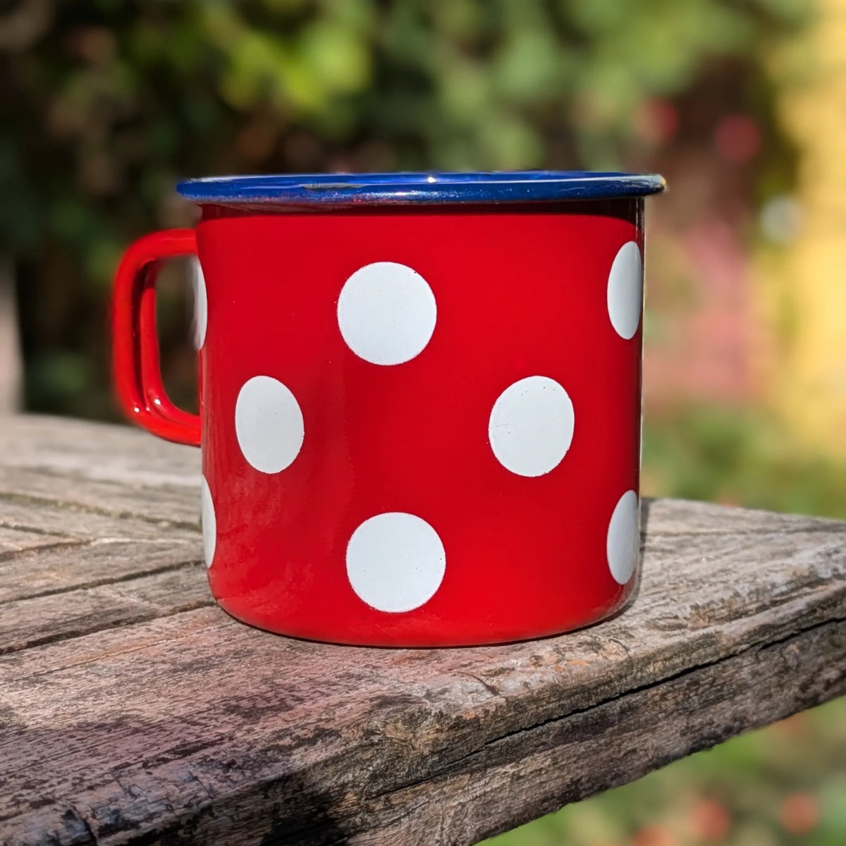 Tasse émaillée rétro rouge à pois blancs posée sur une table