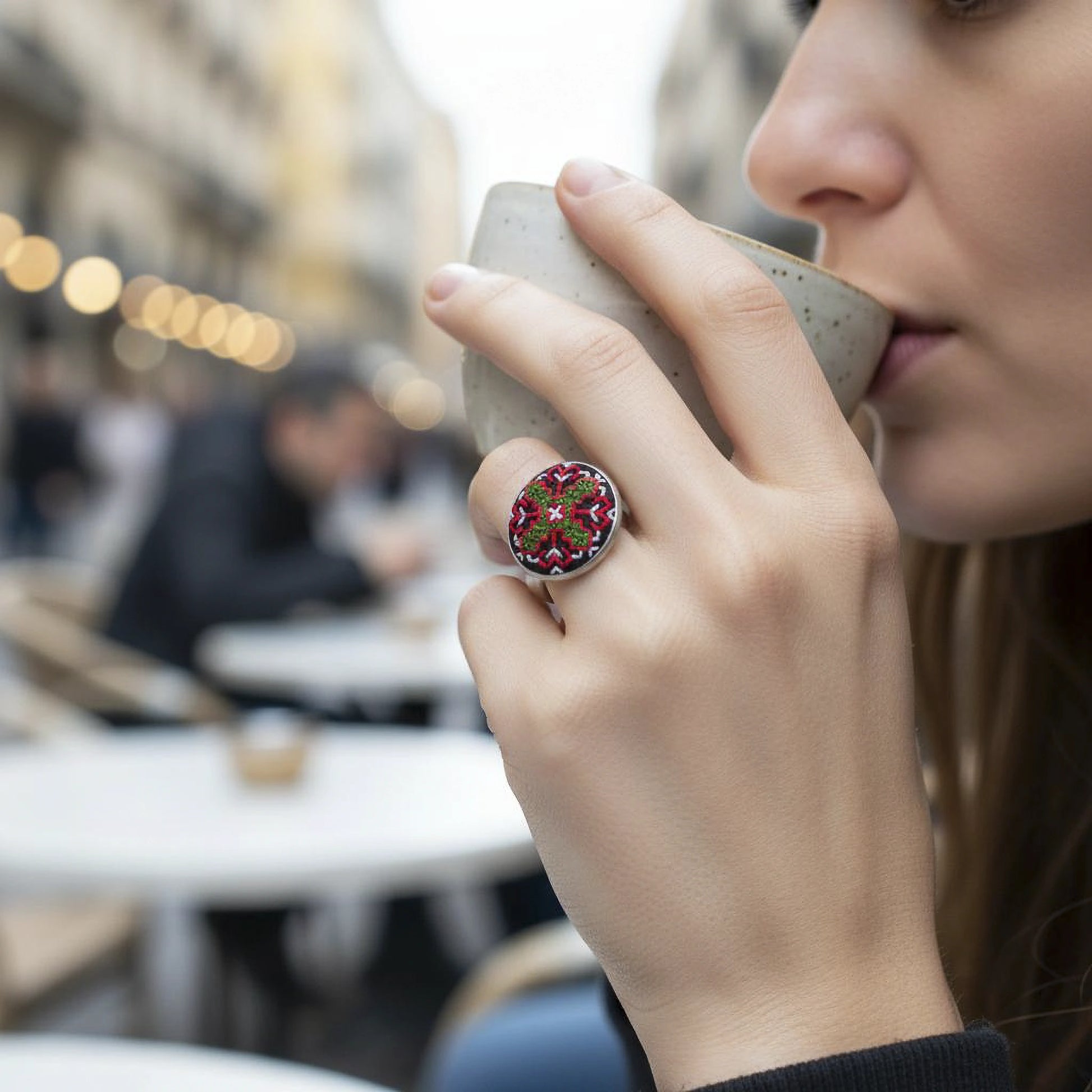 Vue en situation d'une femme portant une bague brodée verte et rouge à fond noir.