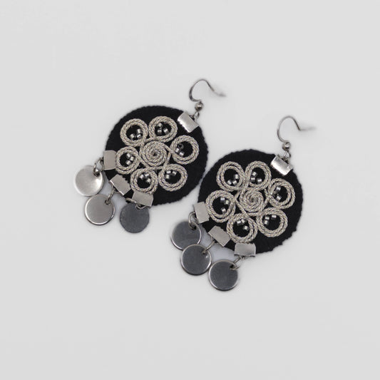 Boucles d’oreilles brodées au fil argenté sur tissu noir, motif spiralé inspiré du folklore serbe. Bijou textile réalisé à la main selon la technique zlatovez. Vue produit sur fond neutre.