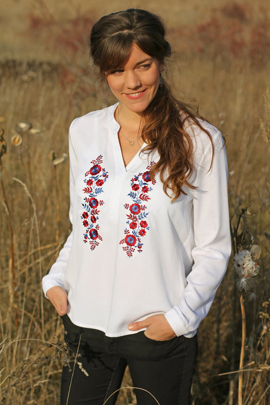 Blouse ample, blanche, avec broderies Palóc rouges et bleues sur le devant. Vue complète du chemisier.