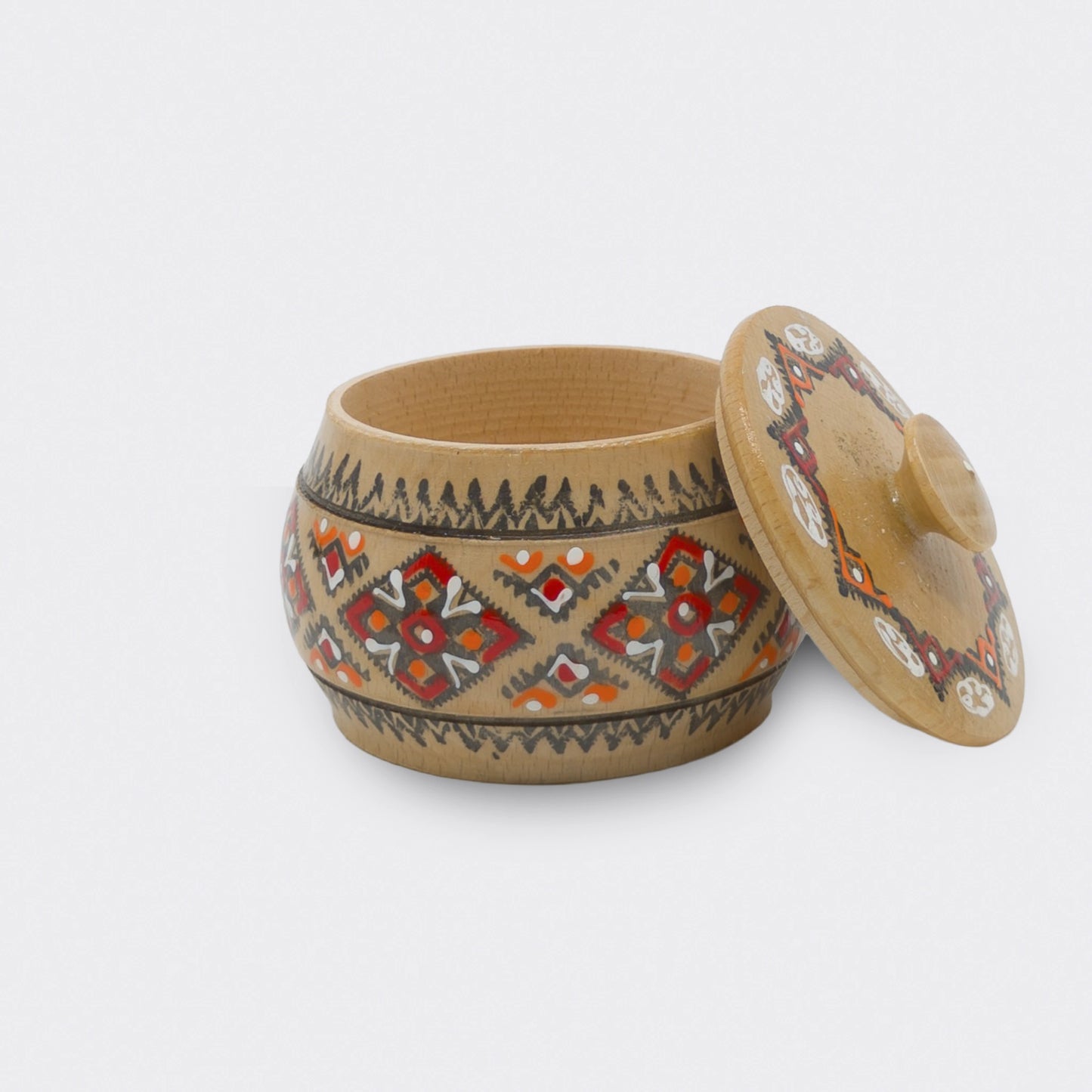 Boîte décorative en bois peinte à la main, vue de côté. Motifs géométriques à dominantes rouges et oranges sur fond bois clair.