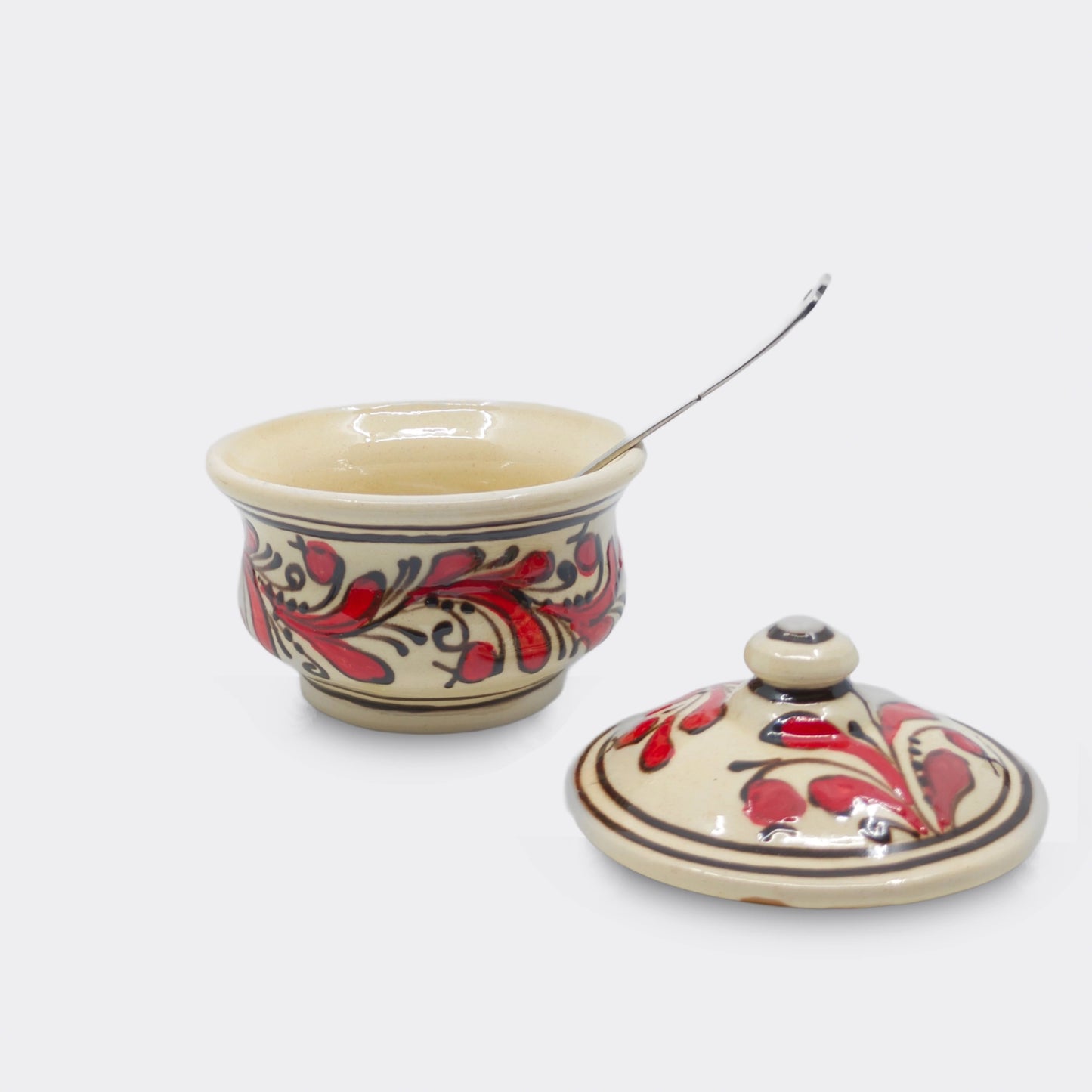 Petite boîte ronde en faïence de Corund décorée de motifs floraux rouges stylisés.