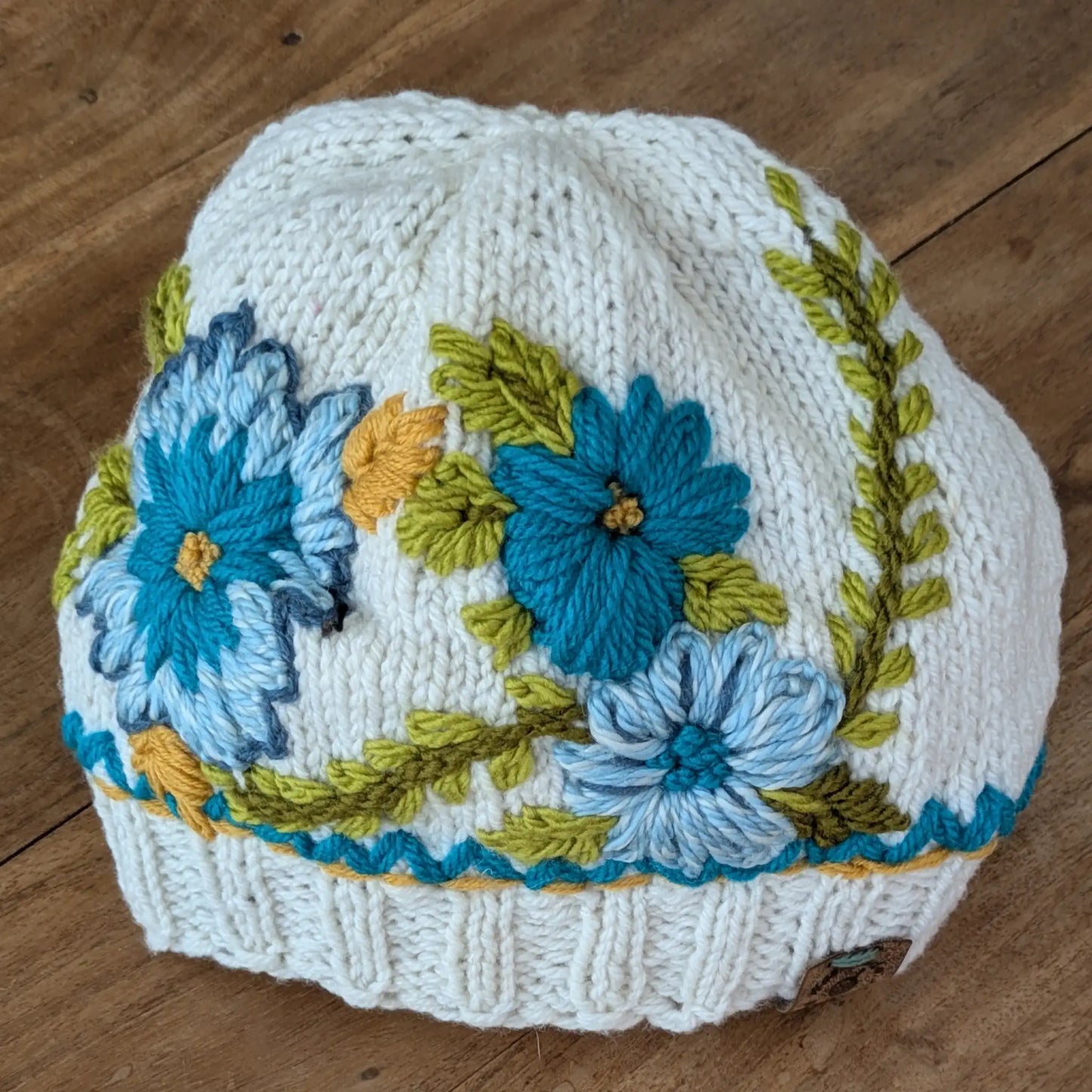 Bonnet blanc cassé tricoté main avec fleurs bleues et turquoise et broderies végétales.