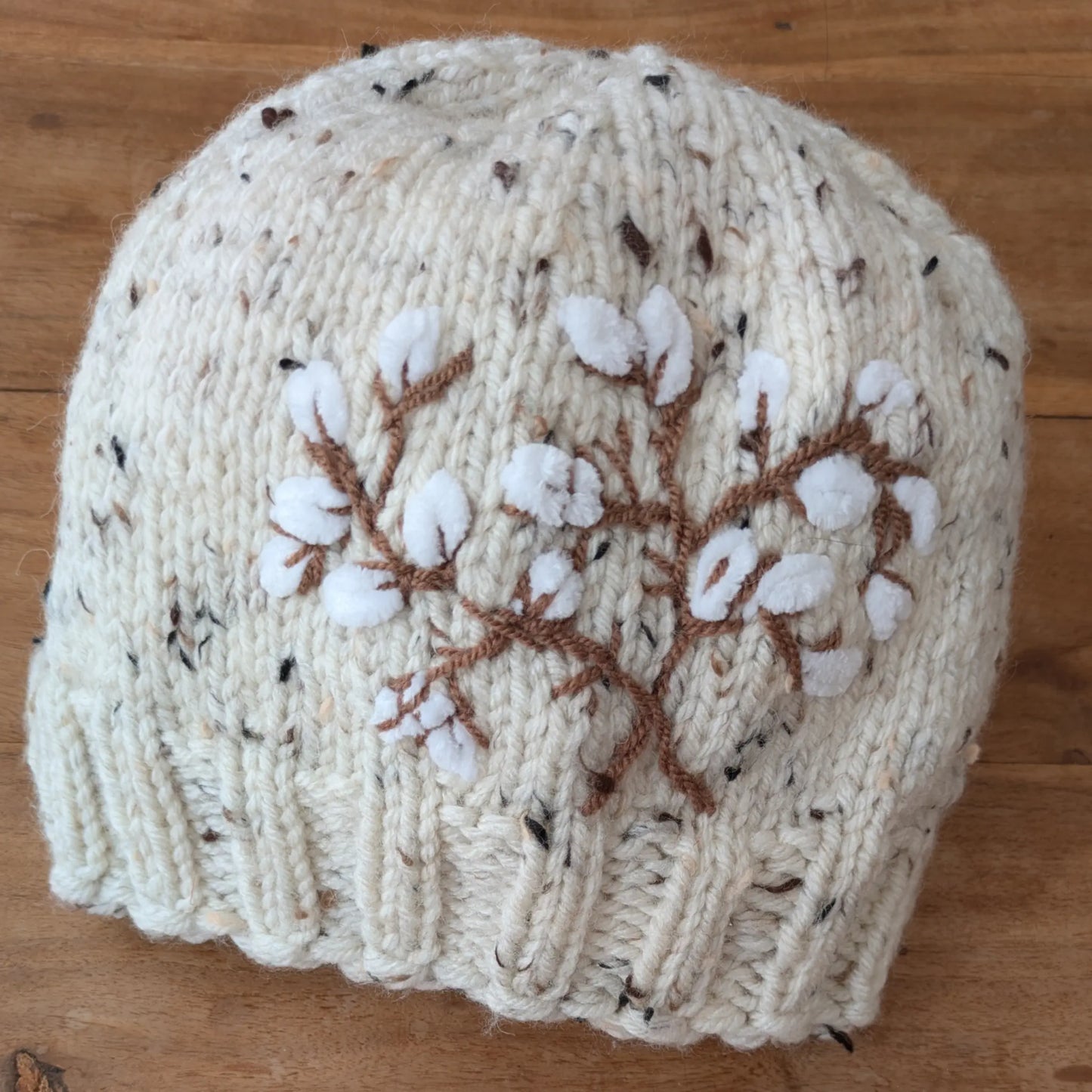 Bonnet écru moucheté tricoté main, avec décor de branches de coton stylisées et bord en côtes.