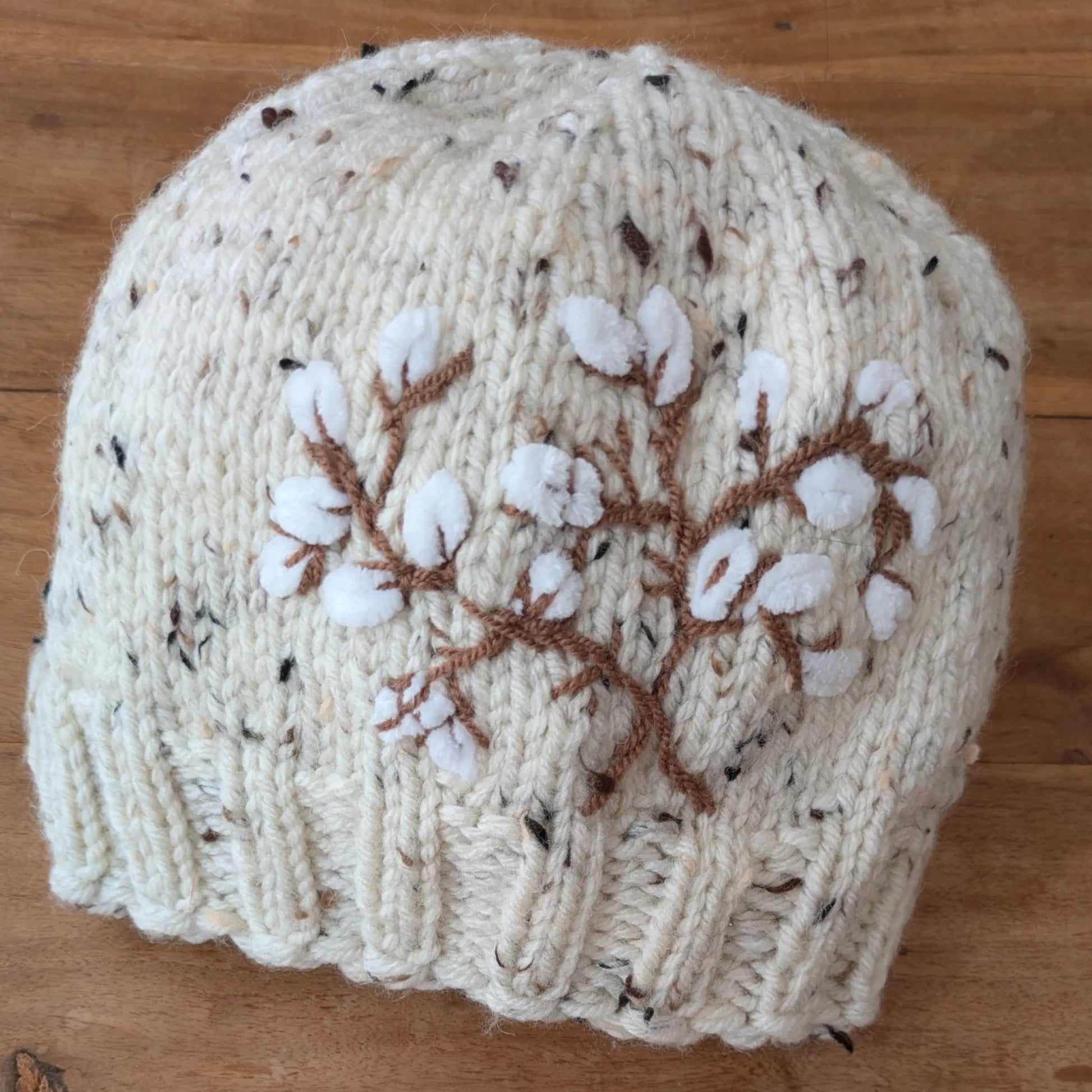 Bonnet écru moucheté tricoté main, avec décor de branches de coton stylisées et bord en côtes.