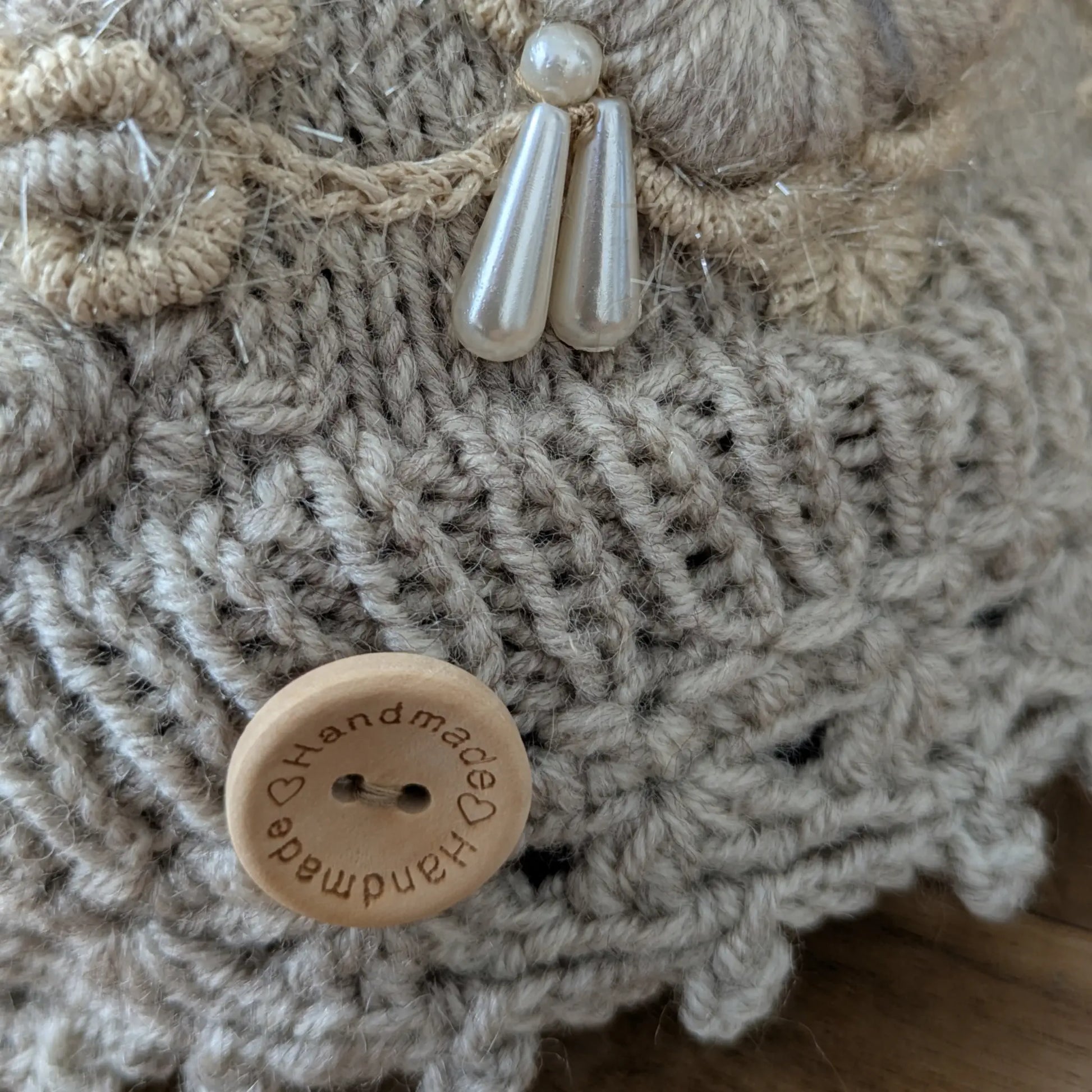 Détail du bouton écru et du décor floral en relief sur le bonnet gris clair tricoté main.
