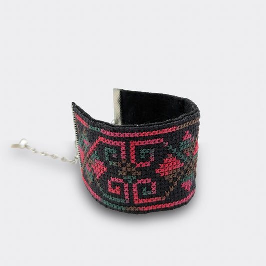 Bracelet artisanal grenadine et vert en broderie serbe, réalisé sur toile Panama avec attaches en acier chirurgical, photographié posé et enroulé sur une surface plane