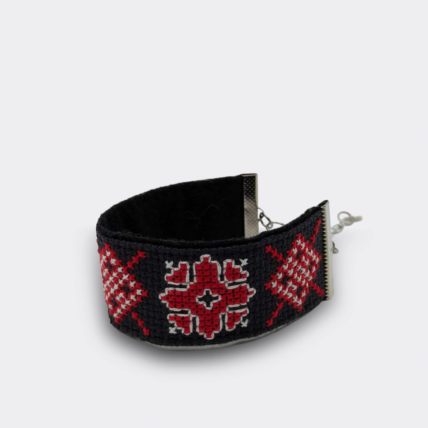 Bracelet en broderie rouge vif sur fond noir, décoré de formes géométriques ethinques. Pièce faite main en Serbie. Vue du bracelet posé et de profil, enroulé.