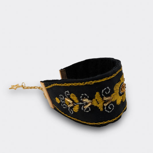 Détail du motif floral central d’un bracelet noir et doré, brodé à la main en point plein et chaînette. Inspiration zlatovez balkanique