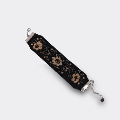 Gros plan sur la broderie champagne d’un bracelet textile noir, décor floral stylisé réalisé à la main. Bijou artisanal serbe, détail du motif, bracelet déplié