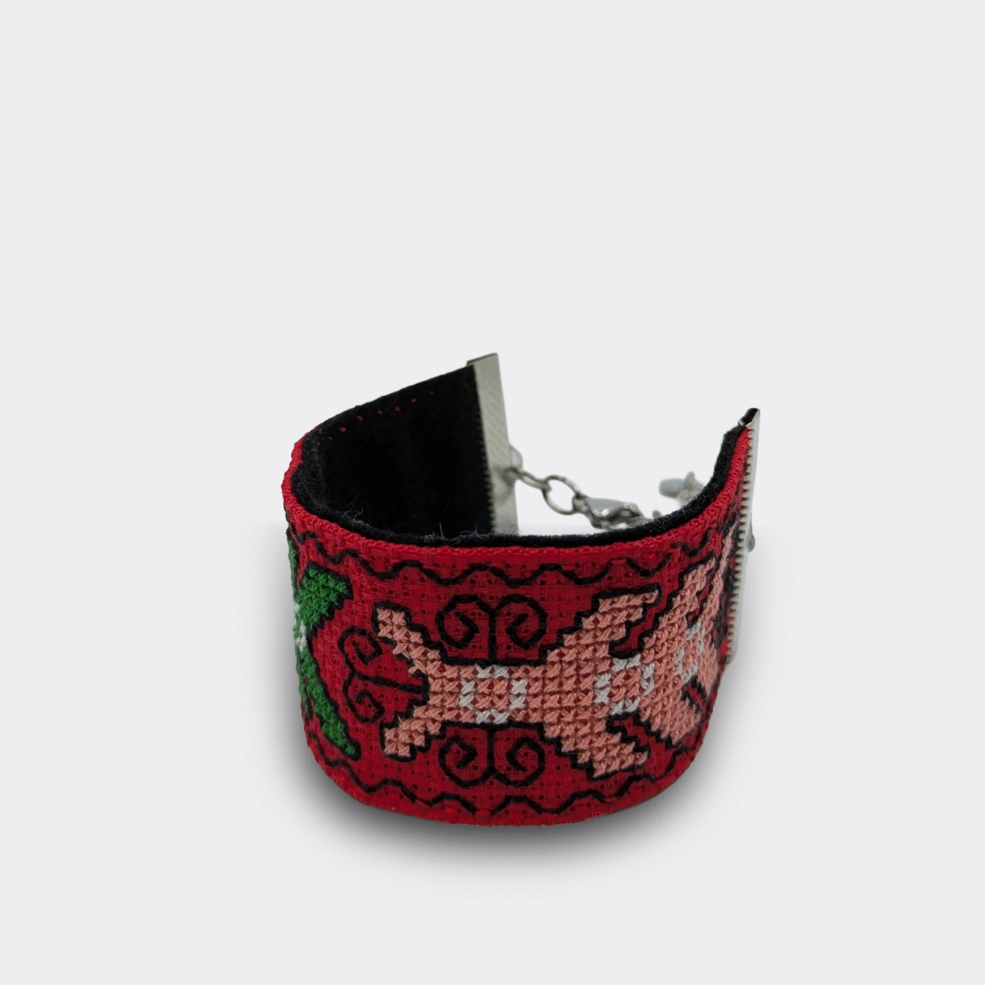 Gros plan sur un bracelet rouge brodé en point croisé, motifs végétaux stylisés en fils verts et roses, vue détaillée