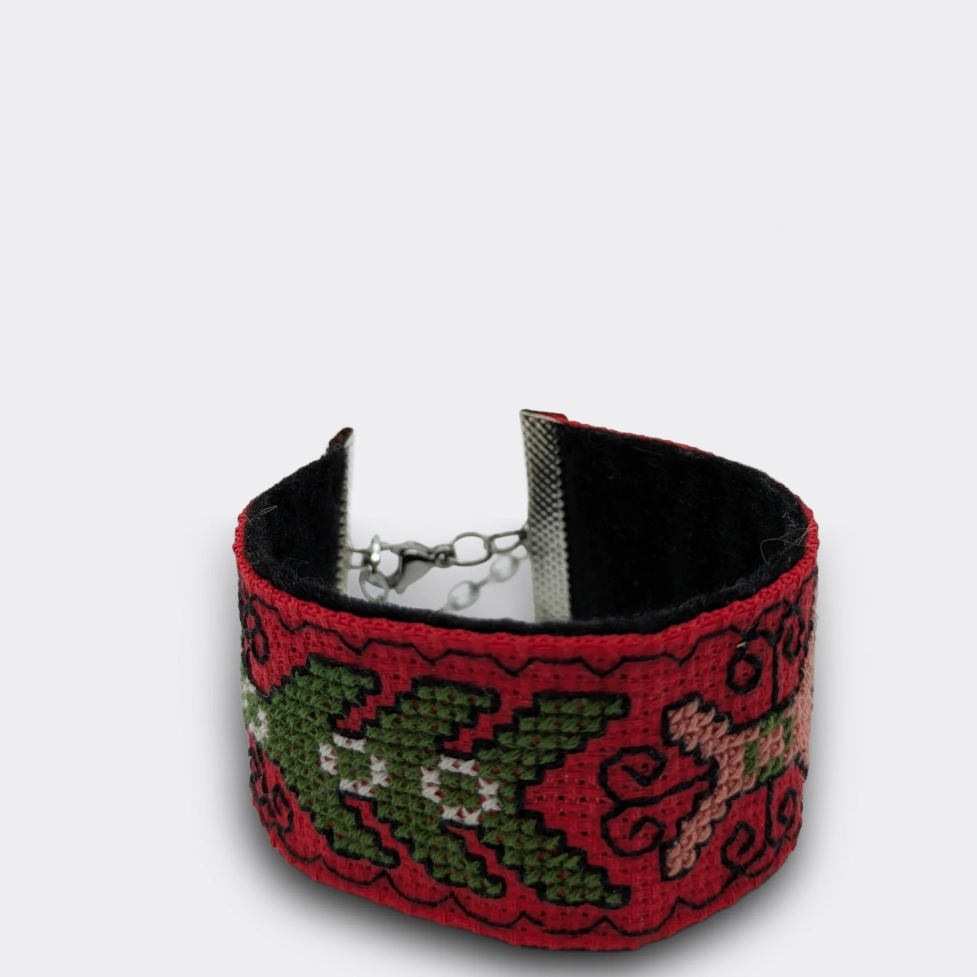 Gros plan sur un bracelet rouge brodé en point croisé, motifs végétaux stylisés en fils verts et roses, attaches métalliques en acier chirurgical