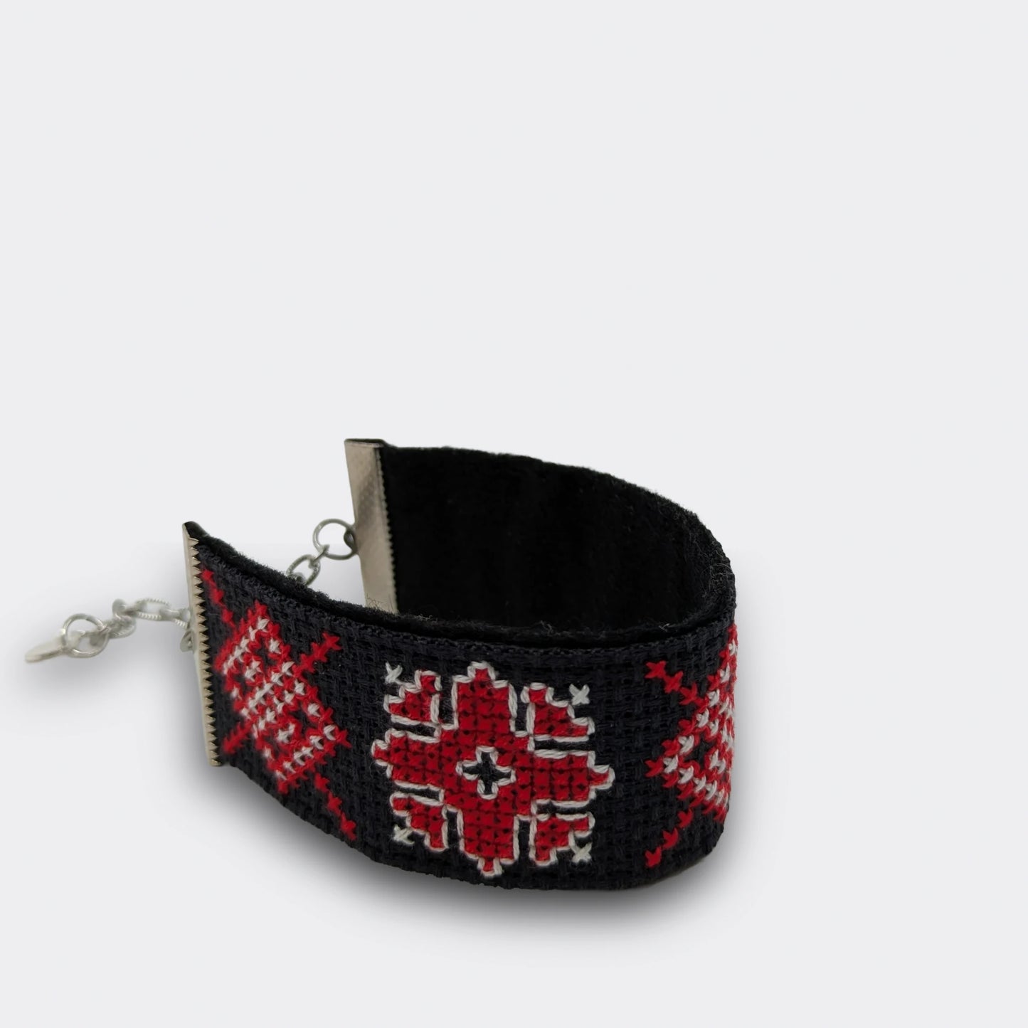 Bracelet en broderie rouge vif sur fond noir, décoré de formes géométriques folkloriques. Pièce faite main en Serbie. Vue du bracelet enroulé et posé.