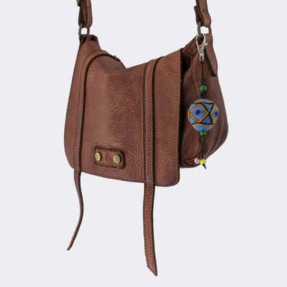 Breloque artisanale serbe en laine bleue feutrée présentée sur un sac en cuir