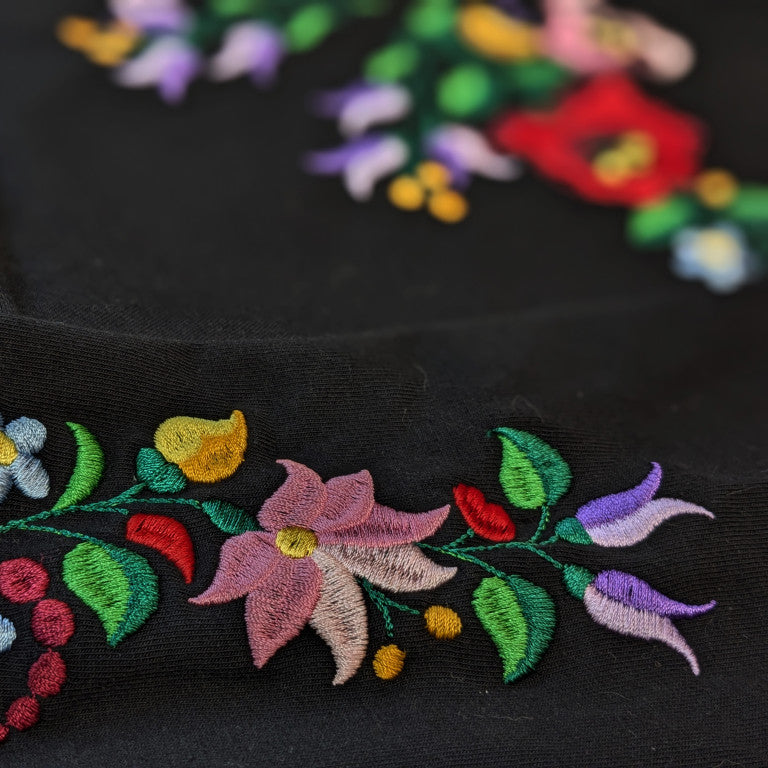 Zoom sur la broderie hongroise traditionnelle Kalocsa. Les couleurs vertes, roses, bleues et rouge ressortent d'autant plus que le fond est noir