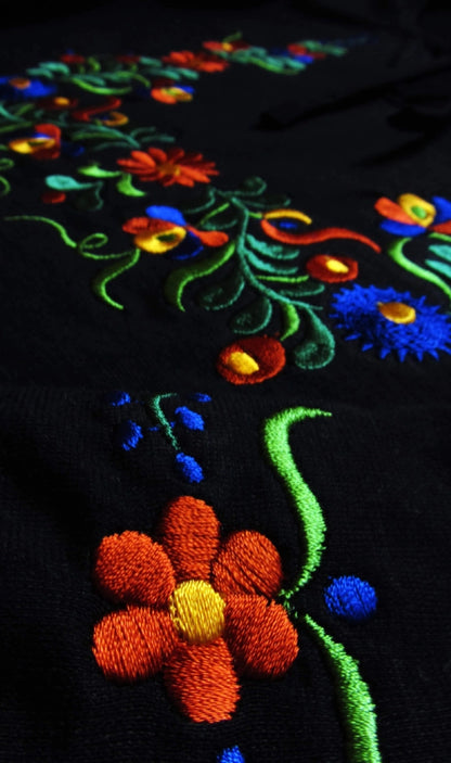 Composition florale aux couleur rouge, bleues et vertes pour cette broderie populaire. Vue de près.