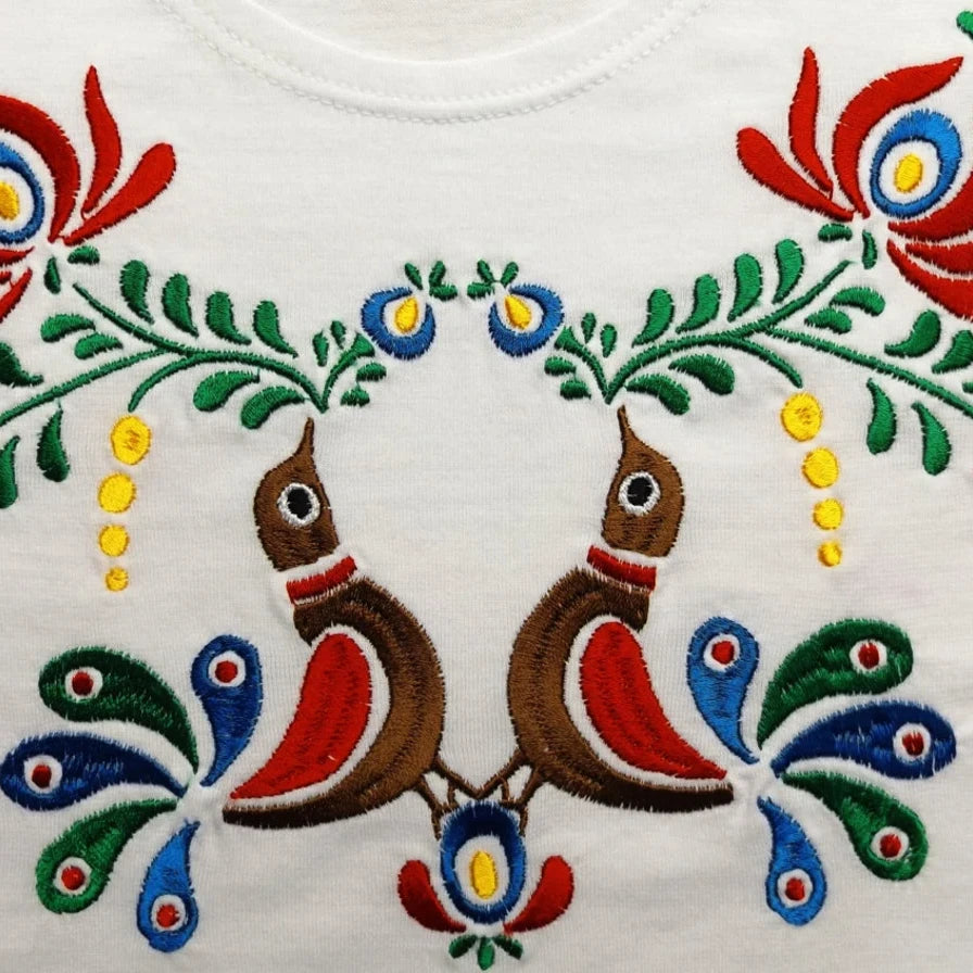 Détail de la broderie du tshirt pour enfant. Deux oiseaux multicolores entourés de fleurs et de feuilles se font face.