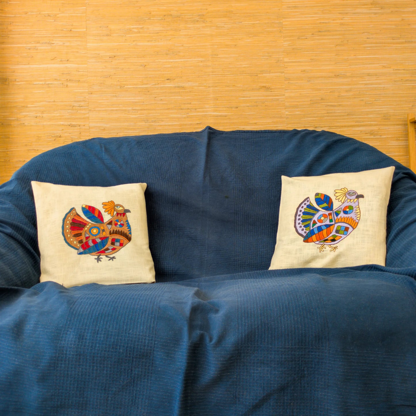 Deux housses de coussin en lin avec une poule brodée bien colorée. Sur un canapé.