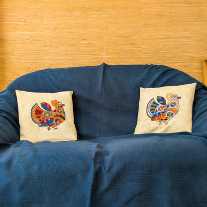 Deux housses de coussin en lin avec une poule brodée bien colorée. Sur un canapé.
