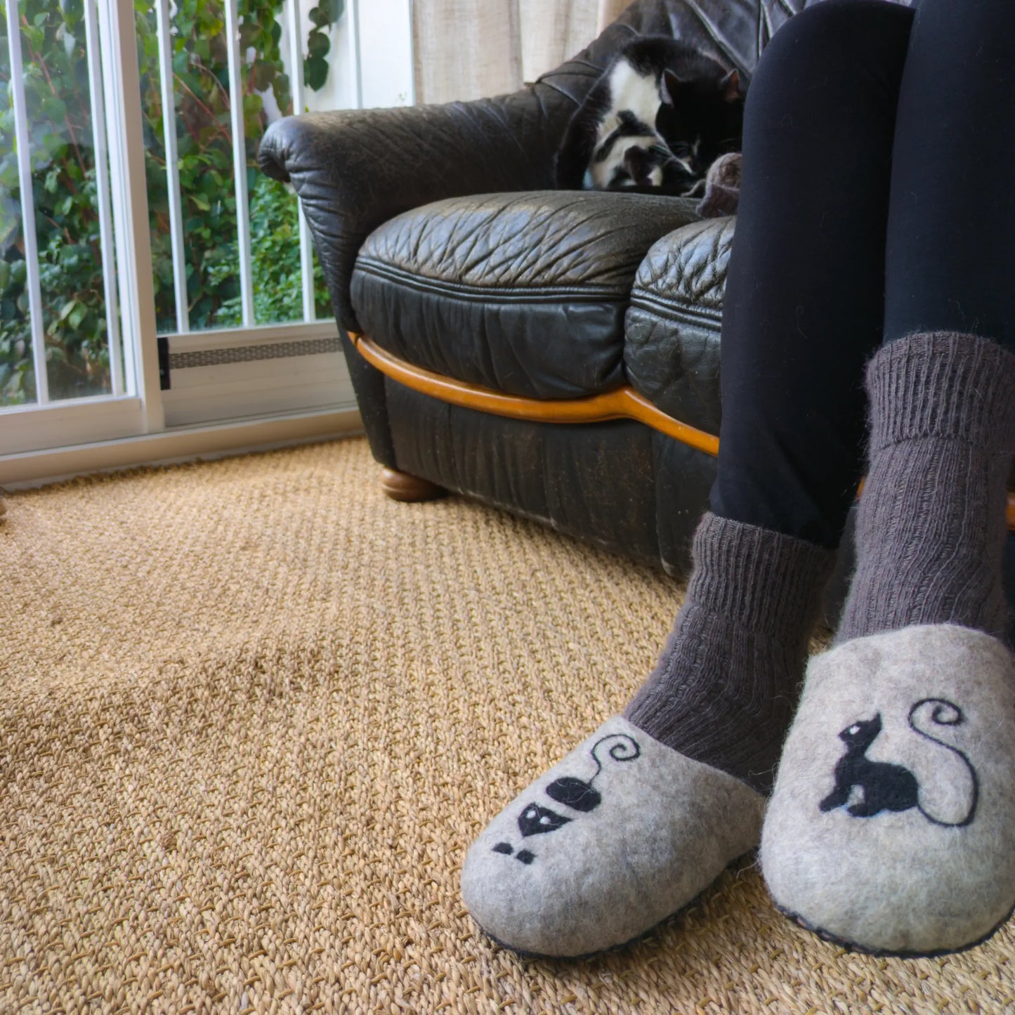 Une personne porte des pantoufles en feutre issu de l'artisanat balkanique. Un chat est dessinée dessus