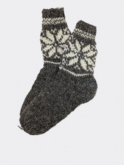 Variante de chaussettes grises en laine de mouton, posées à plat. Le pied est uni et la tige porte un motif écru. Chaussettes épaisses en laine.
