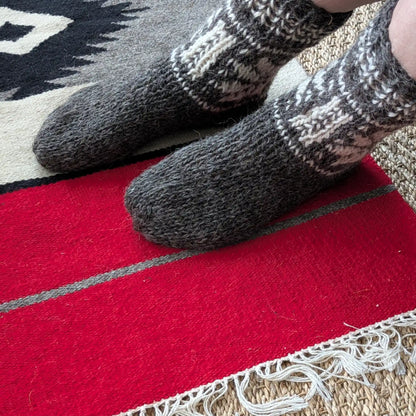 Vue portée de chaussettes en laine de mouton grise. Le haut présente un motif géométrique écru. Une paire épaisse, sans rayures sur le pied.