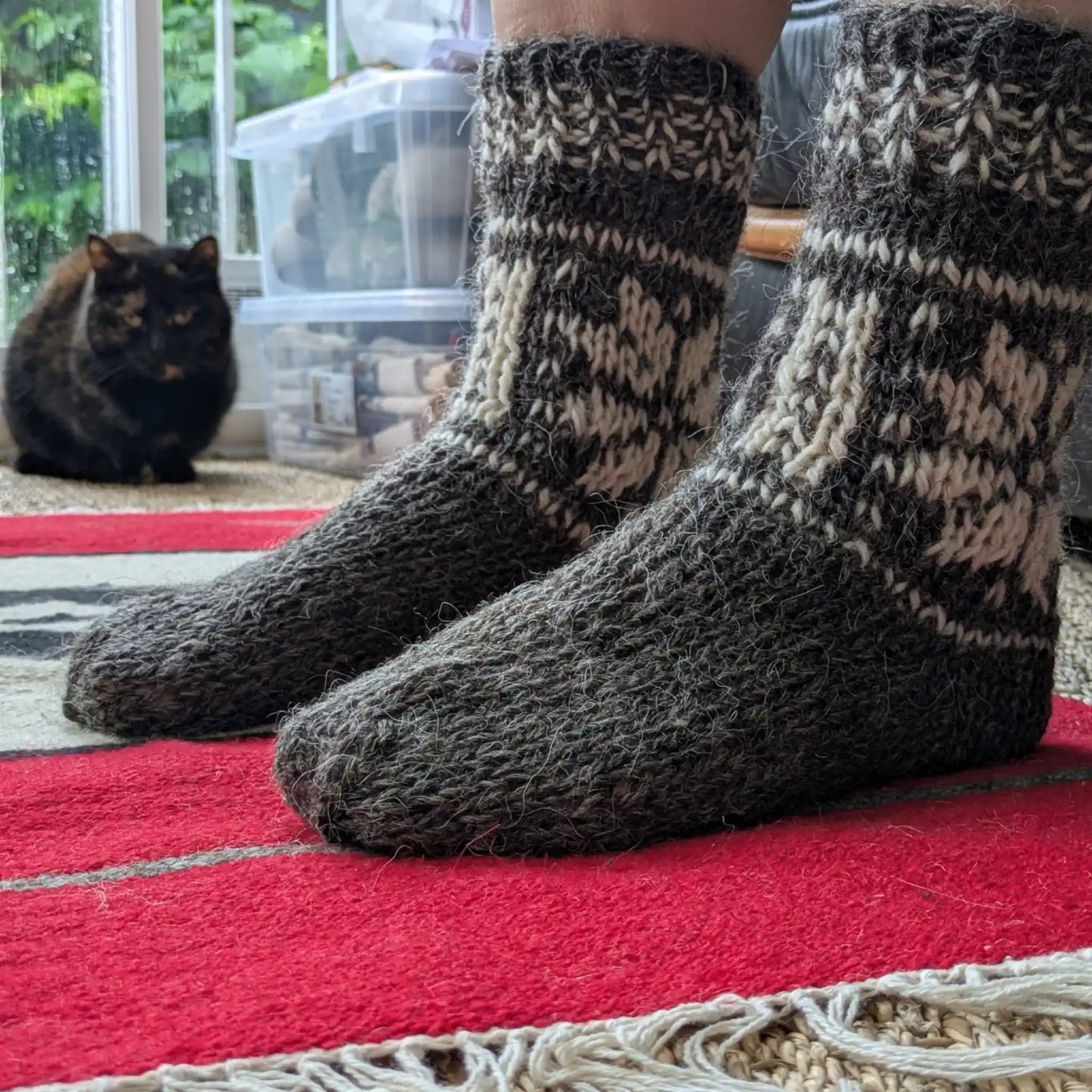 Chaussettes grises en laine de mouton portées en intérieur. Le pied uni contraste avec la tige à motifs écrus. Maille épaisse adaptée aux temps froids.